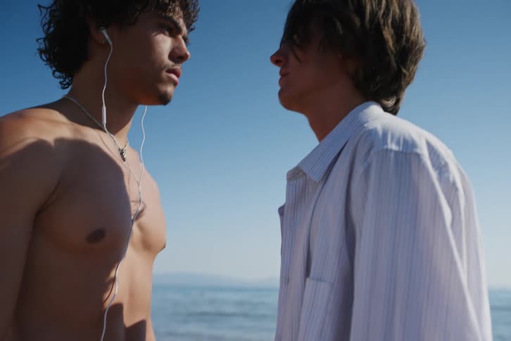 Men walking on beach stop holding hands and stand staring into each others face on a sunny day