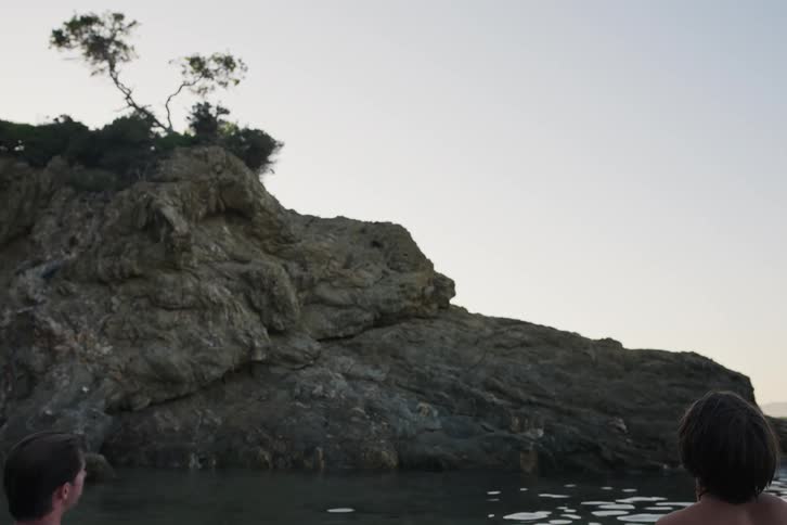 Five men with their backs in the sea and facing a rock begin to swim