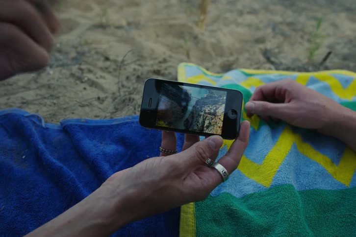 Two people on towels on the sand using a cell phone looking at landscape photographs