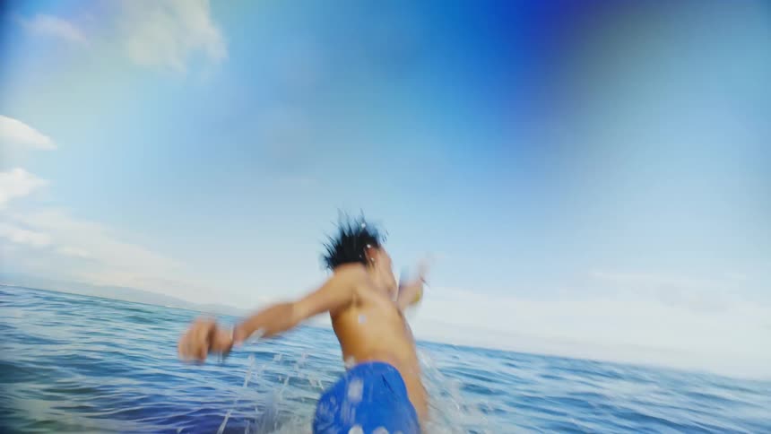 A young man runs through waist high ocean water to try to catch a volleyball