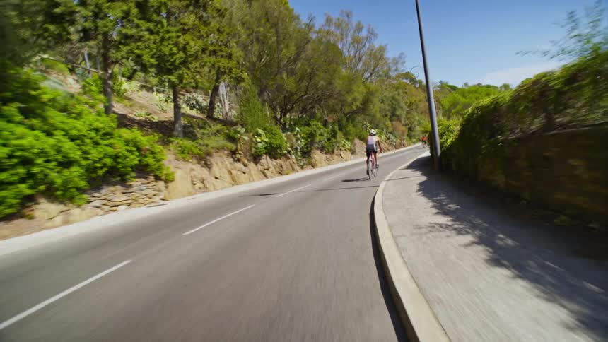 One man passes another cycling down a road with moderate traffic