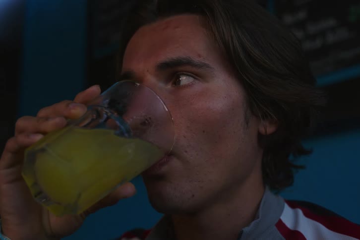 The face of a young man who is looking around suspiciously and then drinks a yellow drink