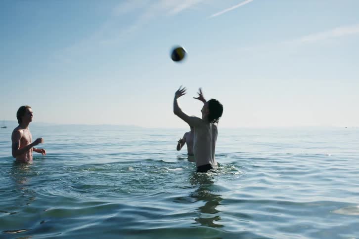 A group of young men tossing a ball around and swimming