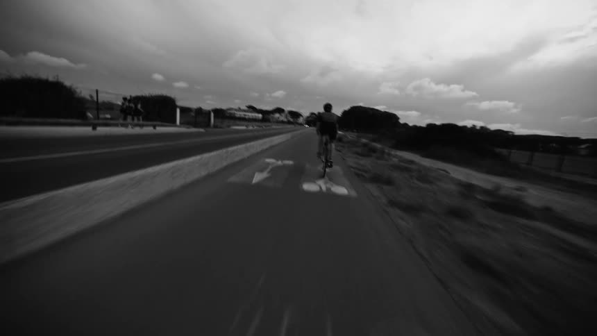 A person riding a bicycle alongside an asphalt street in black and white tones