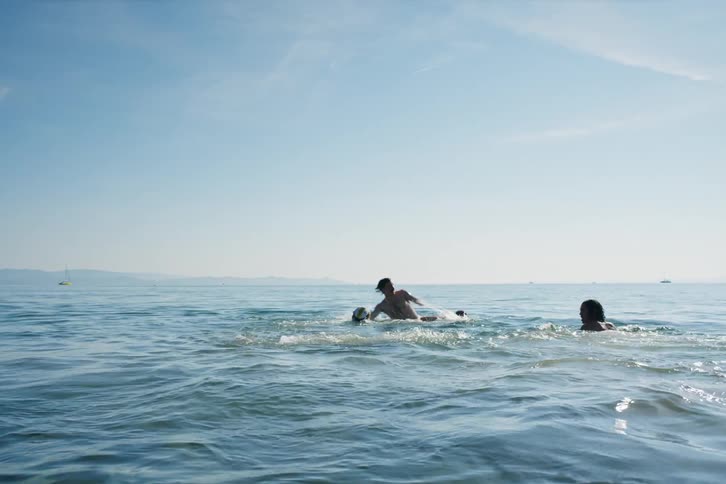 Group of friends in the sea with one of them playing to drown another colleague and playing volleyball