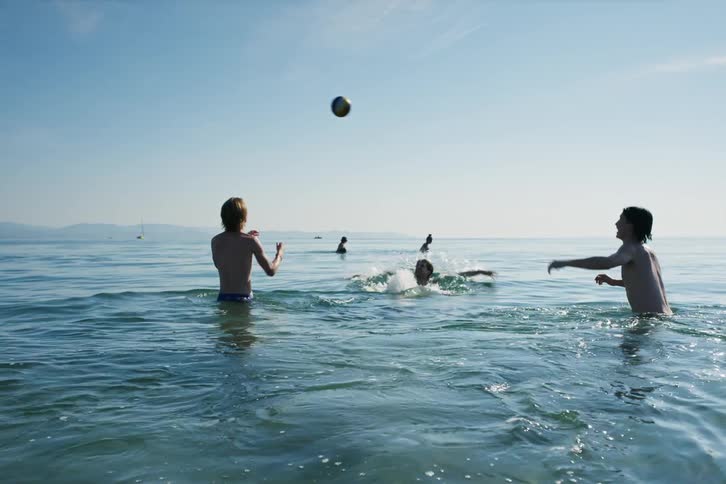A group of male friends swim and knock a ball around in the ocean