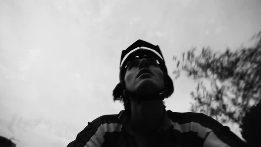 A cyclist who is wearing a helmet who is riding a bicycle in contrast to the sky in black and white tones