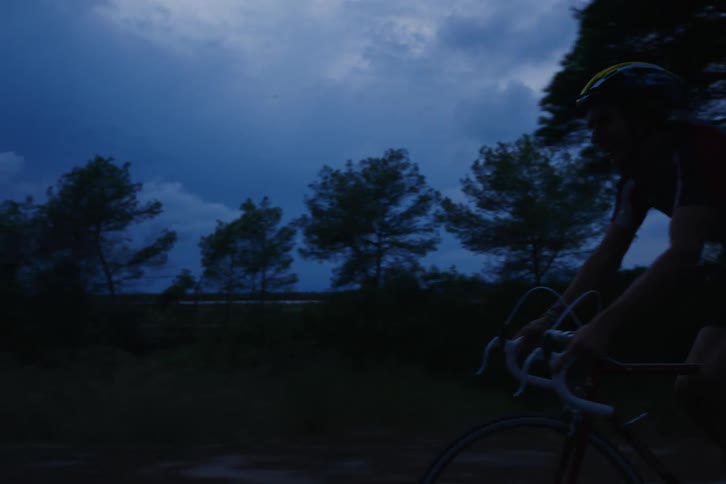 Bicyclists ride down a treelined outdoor path at night