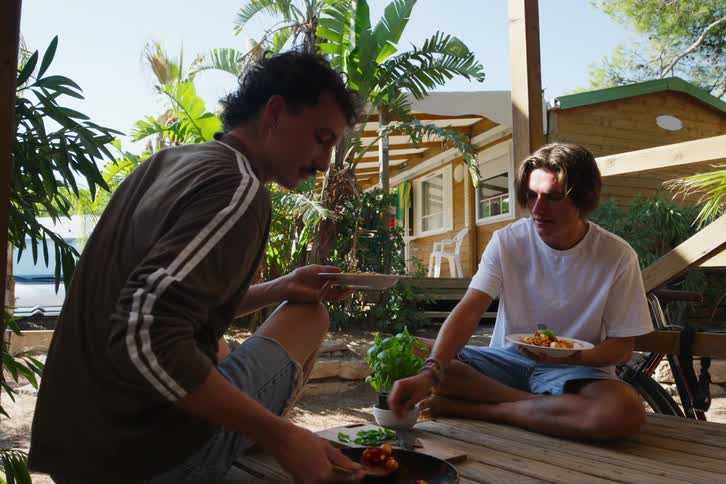 Two friends sitting on a wooden deck serving and eating