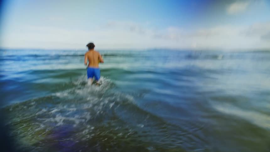 Man running and crossing the waves by the sea holding a ball