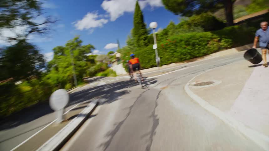 A group of cyclists riding their bikes on an asphalt street with lots of vegetation on the sides in an urban area
