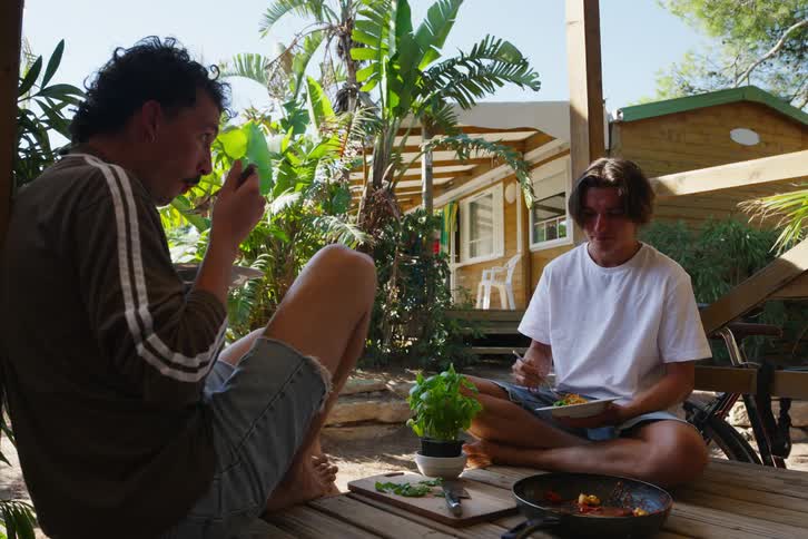 Two young men and friends sitting on a wooden deck while eating