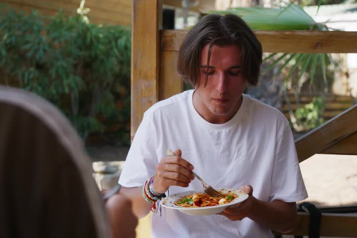 Man sitting eating pasta and talking to his colleague