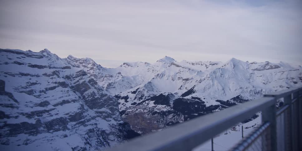 A snowy mountain range beyond a metal fence