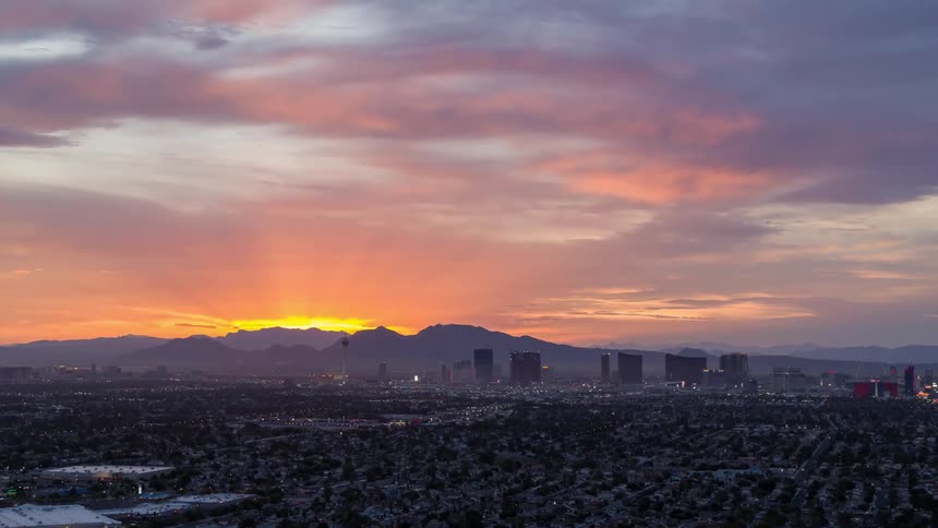 An aerial view of a city with sunlight through the clouds turning the sky orange and pink