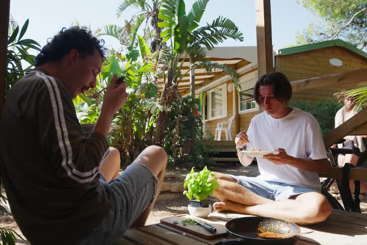Two friends sitting on a wooden deck at a nature resort while having lunch