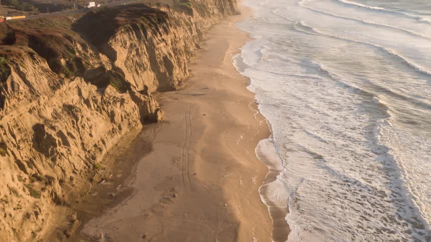 Aerial of waves rolling onto the sandy shoreline along the coast