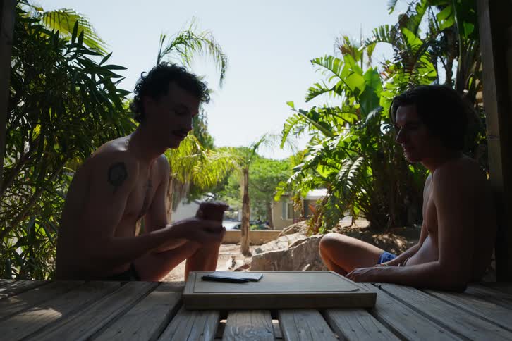 Two male friends sitting outdoors on a wood deck playing dice