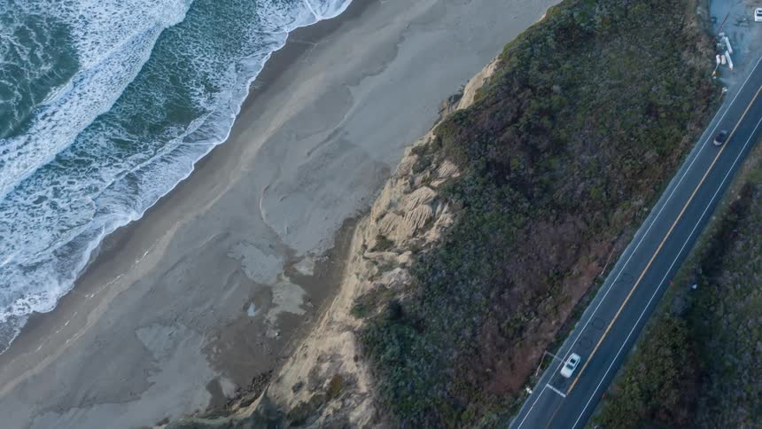 Cars drive on a road next to a mountainous coastal area