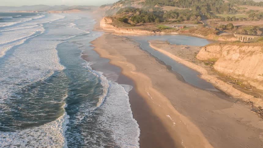 An aerial view of a beach with strong waves breaking on the beach sand
