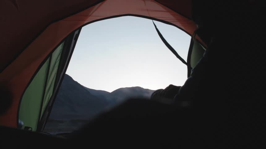 Inside a tent a person wearing thick winter clothes heats up something that produces smoke