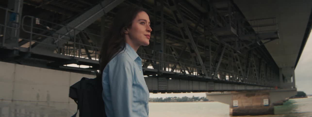 A young woman walking along the seashore with a backpack and a formal tshirt