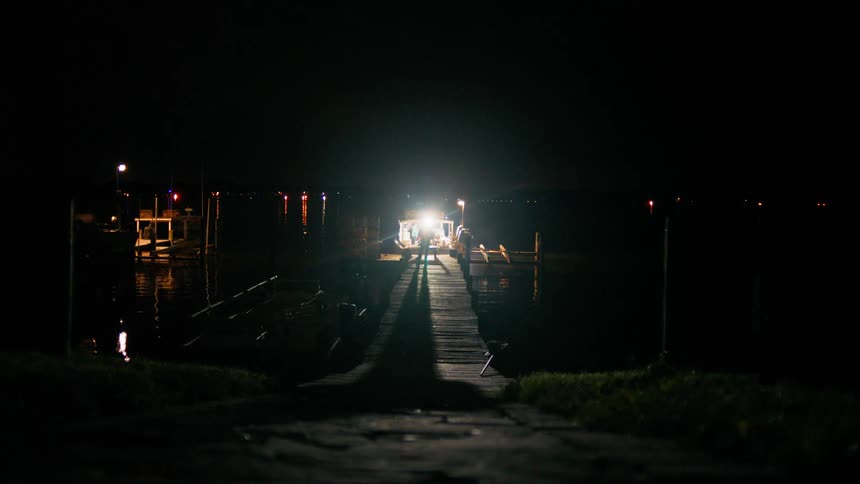 A person stands in front of a bright light on a boat dock