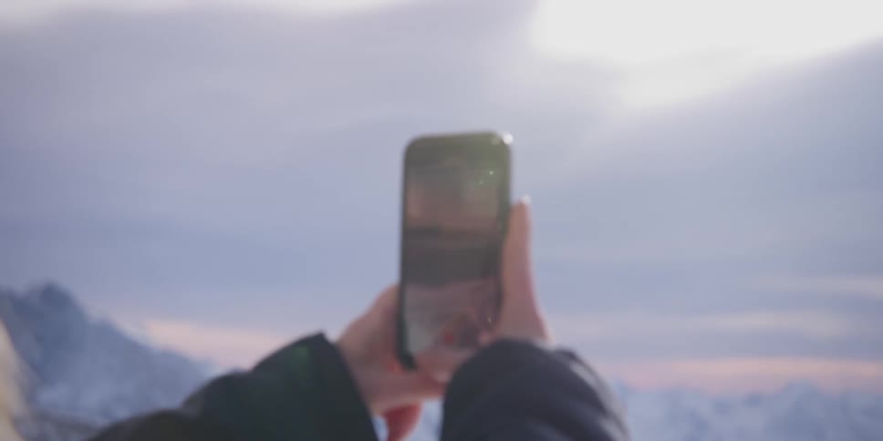 A person is filming a snowcovered mountain range with a cell phone