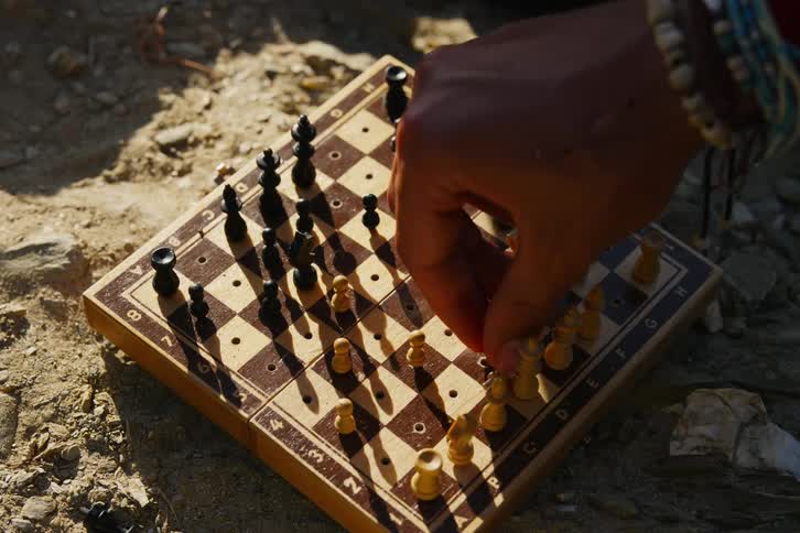 Hands of men playing chess on a rock with sun glare