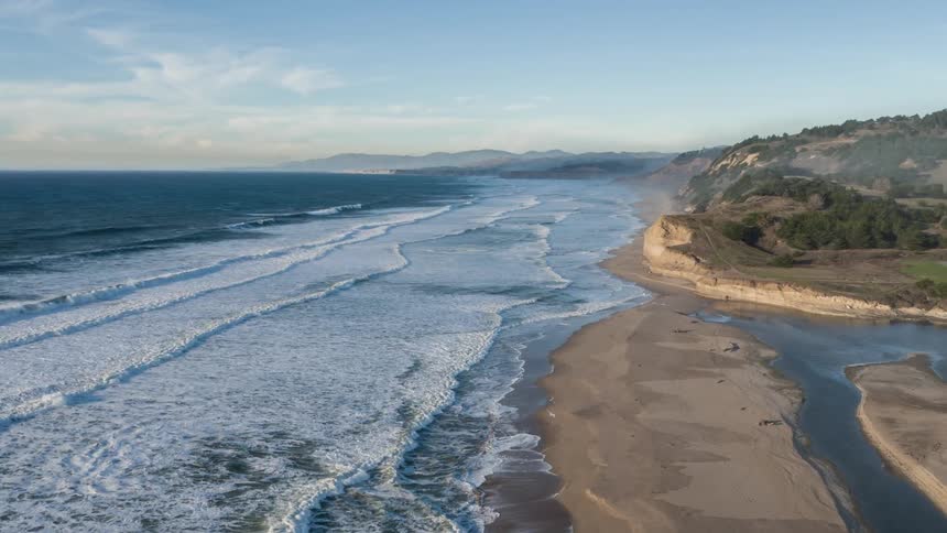 Aerial of ocean waves rolling into the shoreline on a partly sunny day