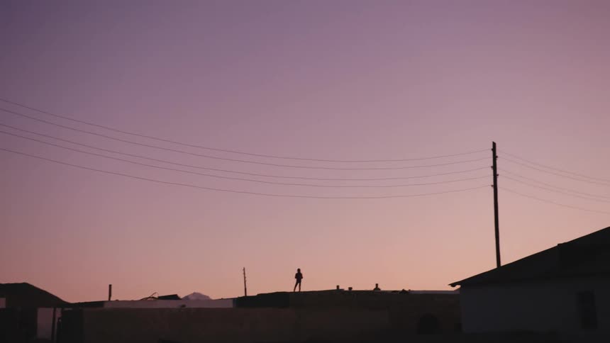 A person stands and turns on a rooftop at sunset