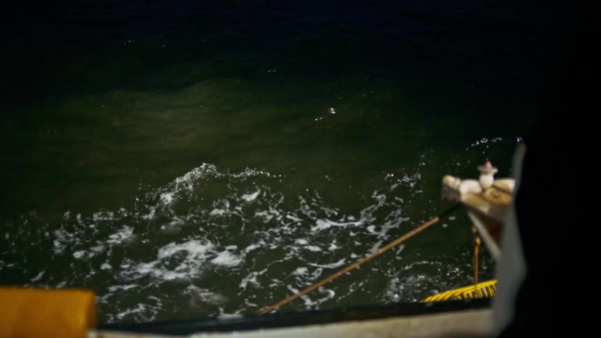 A crab cage floating at the surface of the sea tied with a rope to a boat