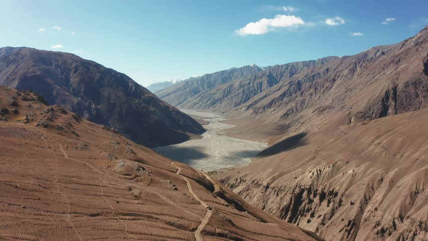 An aerial shot of a canyon between barren brown cliffs in the day