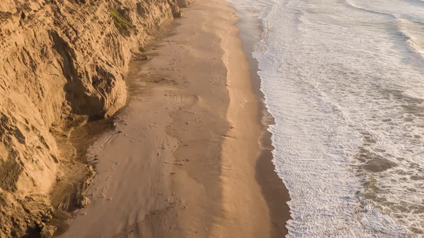 Several ocean waves wash upon a sandy beach located next to cliffs
