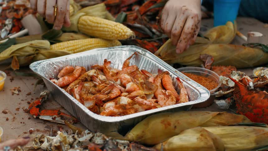 Some human hands are picking up shrimp that are in a metal container