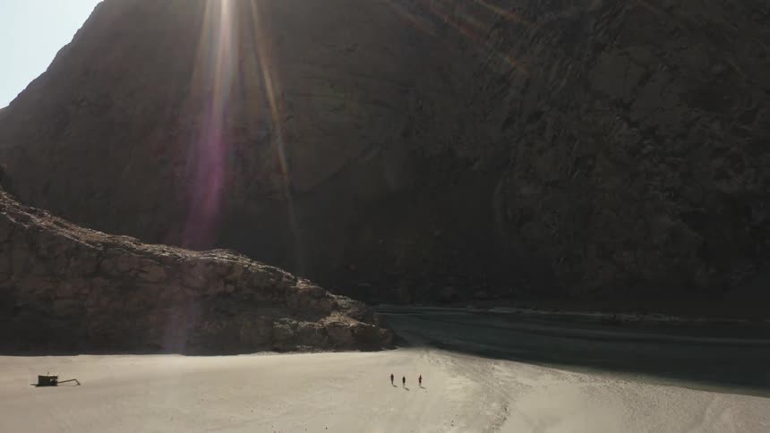 Three people walk across a desert toward a high mountain