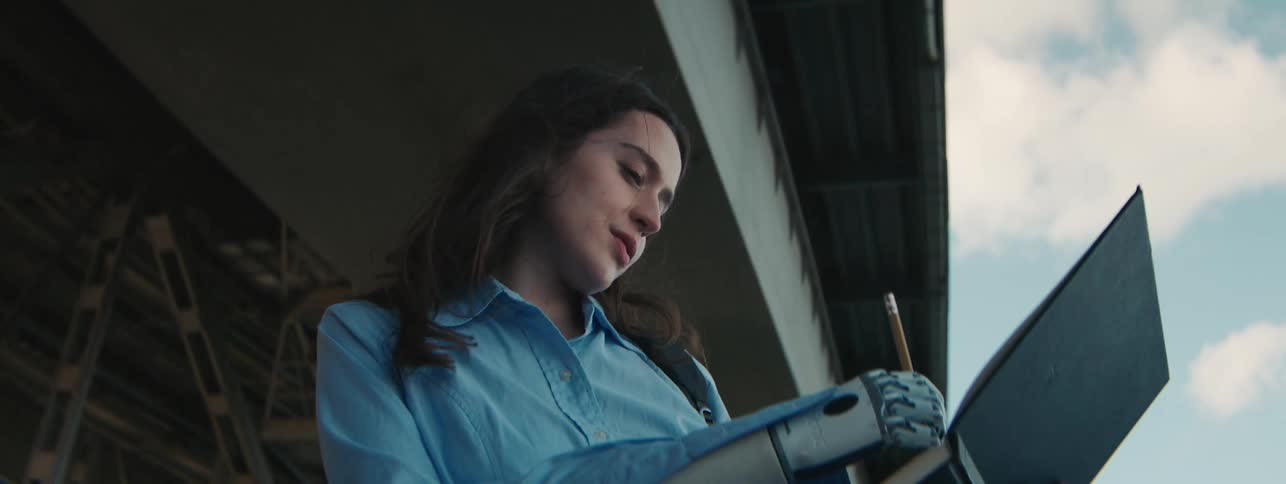 A young woman with a prosthetic arm draws in a back art book