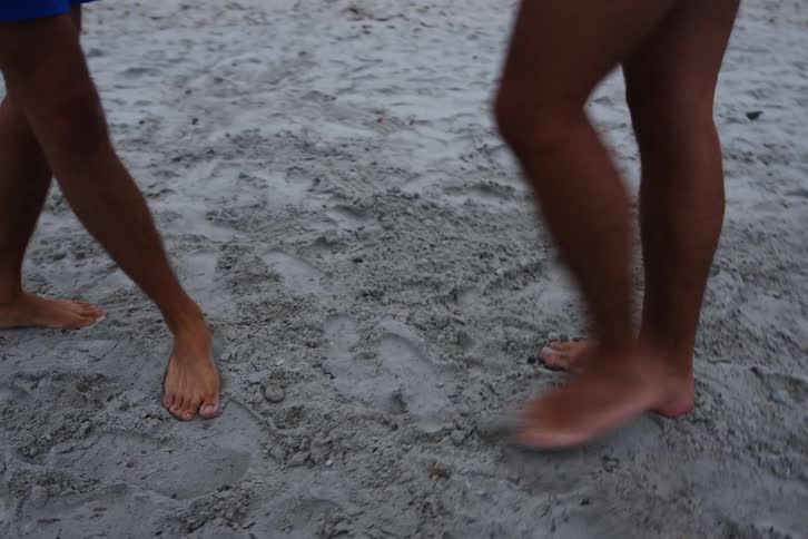 Two young people on the beach sand one of them learning dance steps