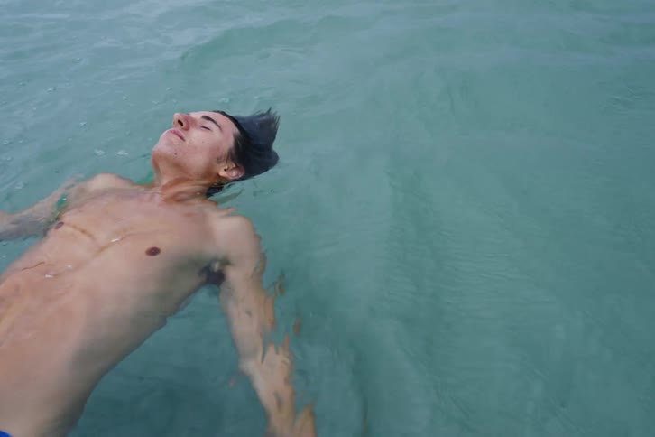 Male wearing blue swimshorts floating in water