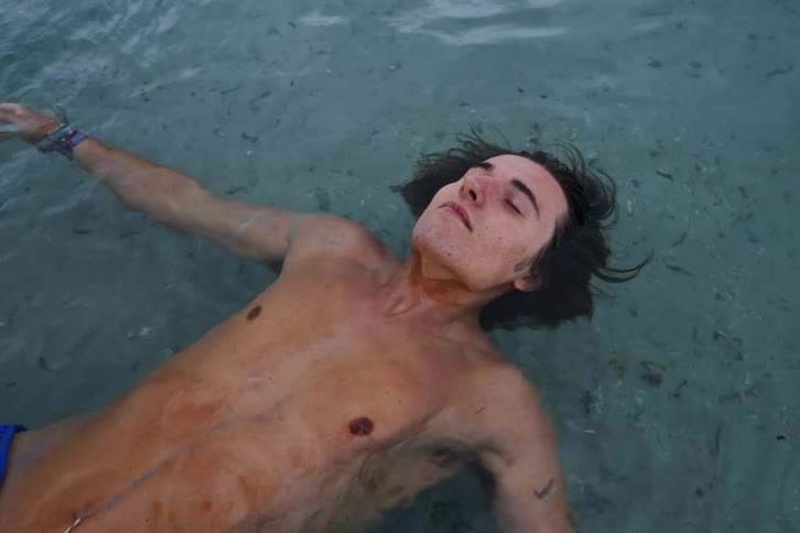 A teenage boy floats in the ocean on a coast
