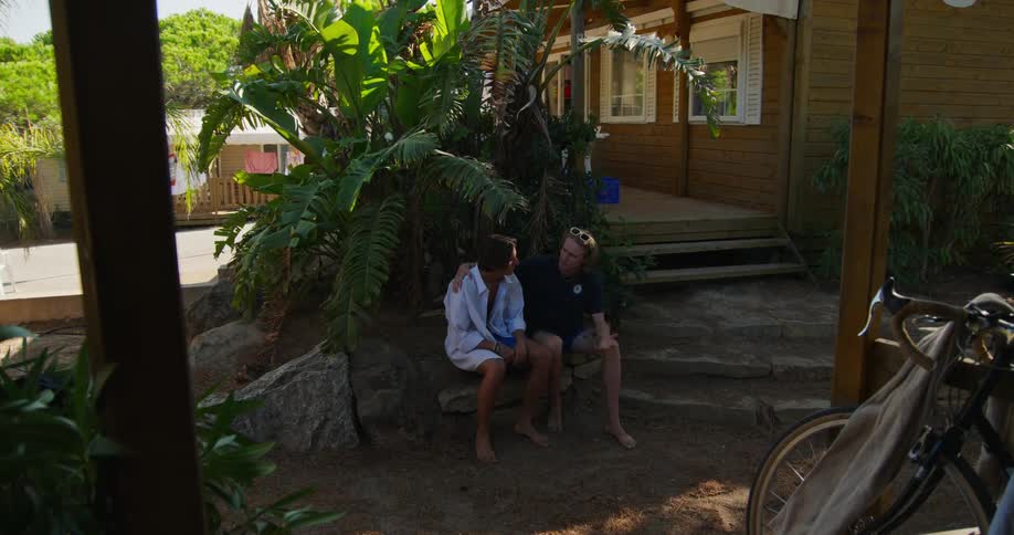 Friends drinking and smoking at a table and two others arriving sitting and enjoying music at a summer resort