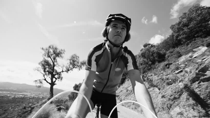 A young man cycling down a dirt road near a cliff in black and white