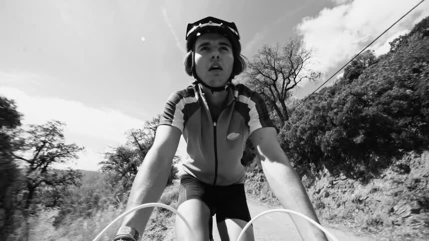 Man cyclist cycling on a narrow road surrounded by mountains and forests during the day