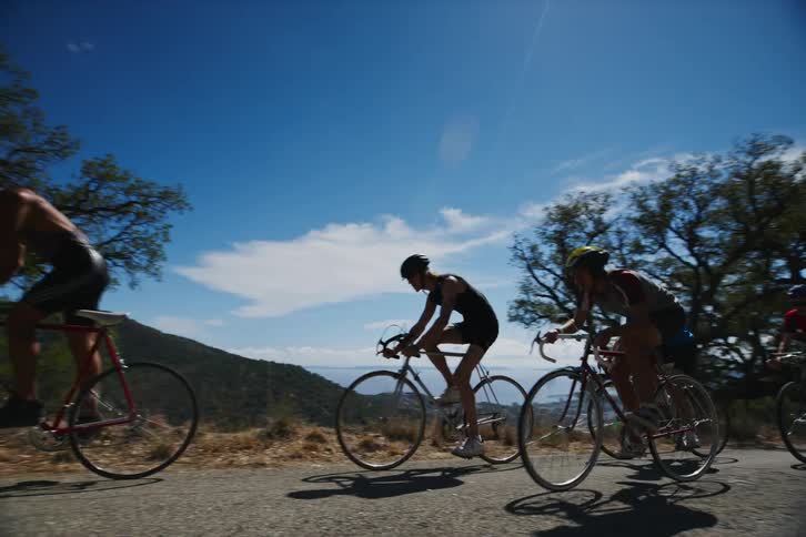 Five male cyclists cycling on a road in the natural environment surrounded by greenery during the day