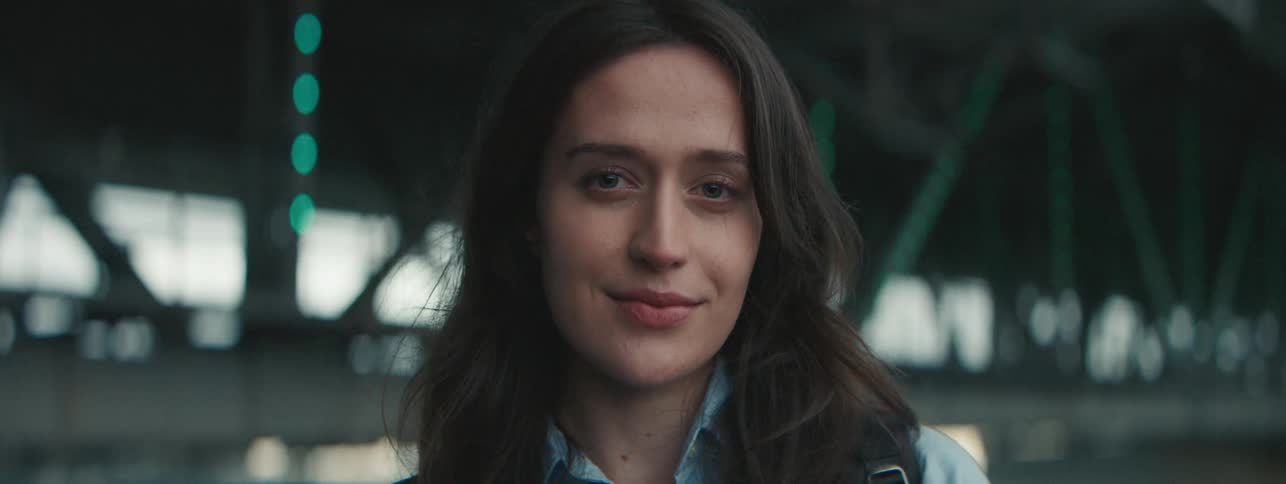 A young woman slightly smiling near a bridge
