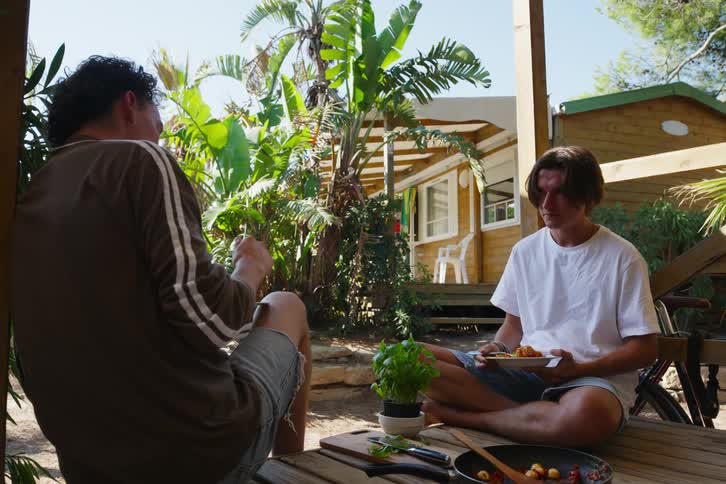 Friends sitting on a wooden deck while eating pasta