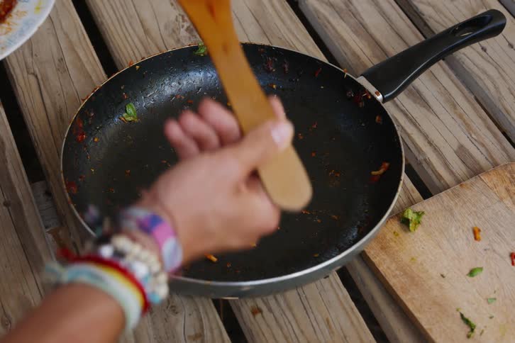 A person holding a wooden spoon scooping food from a frying pan