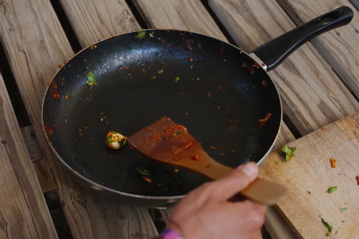 A person serves themselves some food from a pan using a large wooden spoon