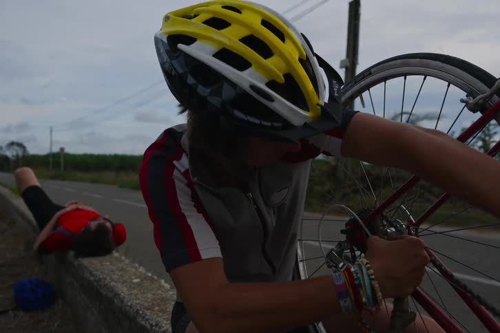 Man repairing his bicycle on the side of the road when his friends continue to pedal