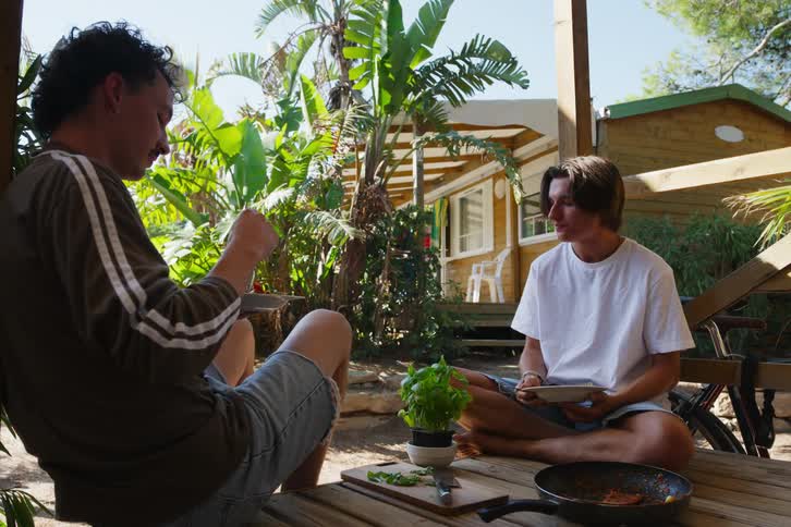 Two friends sitting on a deck helping themselves and eating pasta